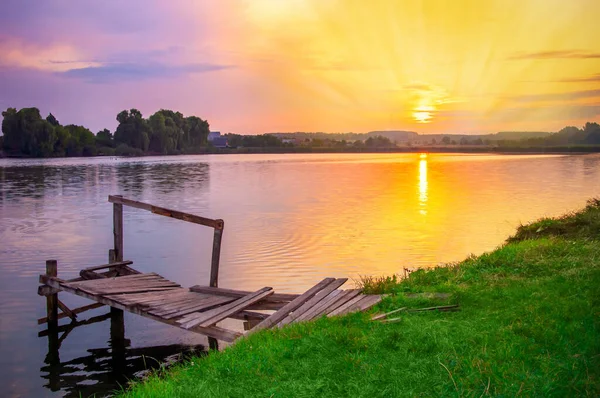 sunrise on the lake in the village. Beautiful setting sun. An old wooden fishermans bridge.