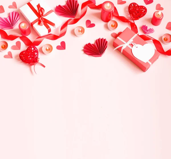 Sobre un fondo rosa se presentan regalos, velas, corazones de papel y una cinta roja —  Fotos de Stock