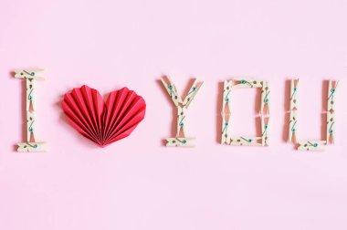 Pembe bir arka planda, tahtadan mandallar ve kırmızı bir kalple kaplanmış tanınma biçiminde bir yazı var.