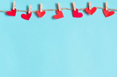 Sevgililer Günü konsepti, mavi arka planda mandallarda asılı kağıt kalpler.