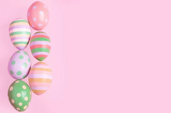 Uova di Pasqua multicolori si trovano sul lato in fila su uno sfondo rosa — Foto Stock