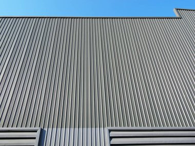 Mavi gökyüzü arka planında güvenlik ve korunma için gri metal levhadan yapılmış bir depo. Asgari modern yapıda çizgili duvar.