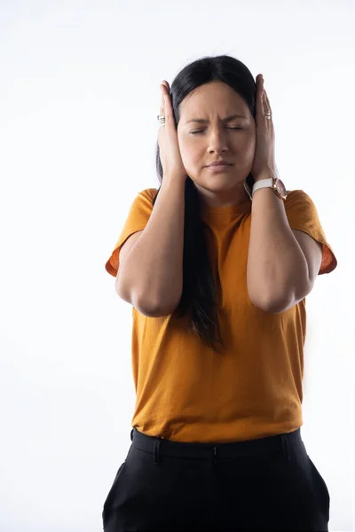 Young Latina girl covers her ears and closes her eyes because she wont to listen. Studio portrait on white background. Vertical format