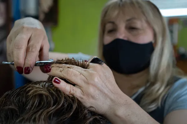 ハサミや櫛で髪を切るフェイスマスクの女性 背景がぼけて — ストック写真