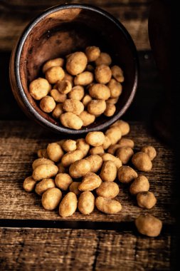 Coated salted peanuts in a brown bowl on a dark background, ideal to accompany beer.