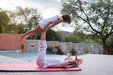 Mother balancing her daughter on her legs in the backyard of the house.