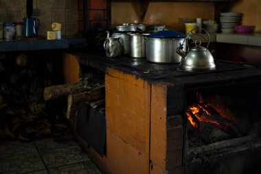 Traditional kitchen with wood stove burning and metal pots. Blurred background, copy space.