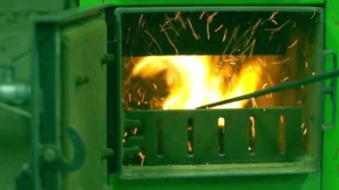 Uzun saplı metal kepçeler özel evi ısıtmak için kömür kazanının ocağında kömür karıştırıyor, parlak ateş, yanma odasından kıvılcımlar çıkıyor. Kışın kömür ısınması