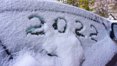 Karla kaplı bir arabanın yan camında 2022 rakamları var. Yeni yıl 2022, soğuk kış, karla kaplı araba.