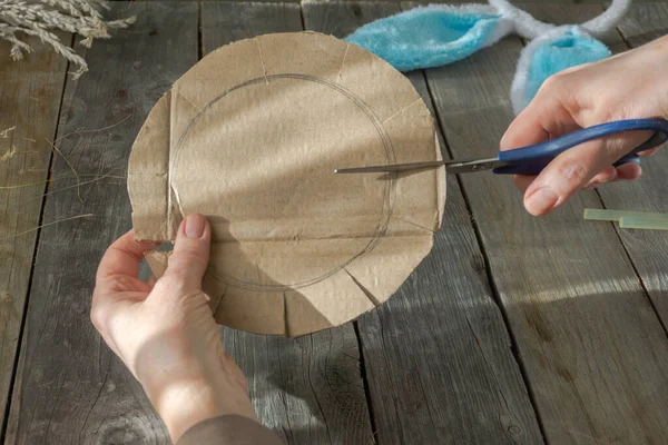 手工制作的主人级复活节鸟巢，由天然干草制成，并使用硬纸板。一位老妇人的手一步一步地展示了如何在木头背景上做一个复活节鸟巢 免版税图库图片