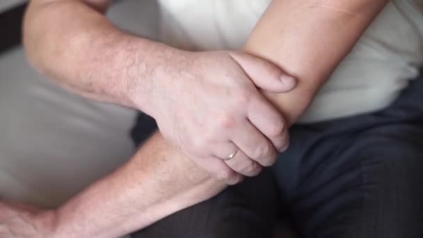 An elderly man in a light T-shirt rubs his sore elbow with his hand. Diseased joints, diseases of the elderly — Stock Video