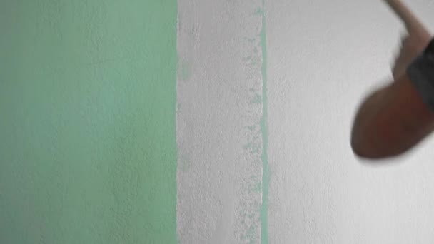 A man repaints the green wall of the room with a roller in a light gray color. Concept repair, painting the walls with your own hands — Stock Video