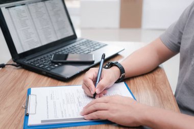 Service staff write on document about car repairs and use laptop online check part list on table in office