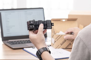 Elinizi kapatın. Bir adam yedek parçaların bulunduğu kutudan elektrikli araba pencerelerini ayarlamak için düğme setini tutun ve araba servisindeki müşterilere geçmeden önce dizüstü bilgisayarın doğruluğunu kontrol edin. 