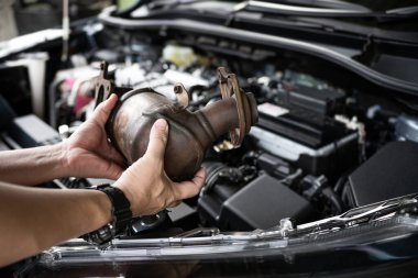 Eldeki eski katalitik dönüştürücüyü kapat. Teknisyen motor benzini tozunu kaldırdı. Arka plandaki motor odası ve servis konseptinde filtrede tıkandı.
