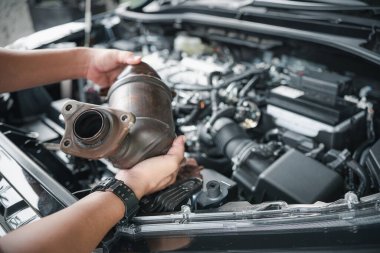 Eldeki eski katalitik dönüştürücüyü kapat. Araba tamircisi motor benzini tozunu kaldırdı. Arka plandaki filtrede tıkanmış durumda.