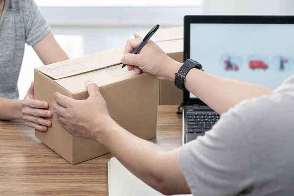 Close up hand a man use pen write on parcel box from women about the parcel delivery address and use laptop to register in the online system