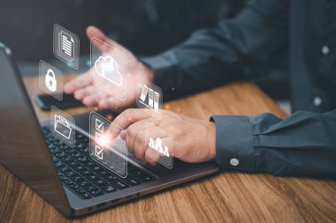 Belge yönetimi ve teknoloji konsepti, İşadamı ofiste çalışan sanal ekranda simgeleri olan bir dizüstü bilgisayar ve koyu çimento duvar arka planı kullanır