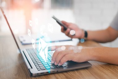 Posta göndermek ve e-posta simgeleri ile ofis masaları üzerinde çalışmak için dizüstü bilgisayar ve akıllı telefonlar kullanan iş adamı, e-posta pazarlama kavramı