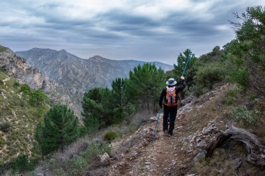 Sierra Almijara ve Tejeda 'da çam ağaçları ve fırtınalı bir gökyüzü olan bir patikada yürüyen bir yürüyüşçü.