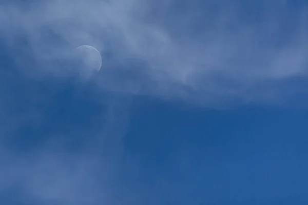 The waning moon between clouds in a blue sky. Nature.