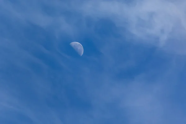 The waning moon between clouds in a blue sky. Nature.