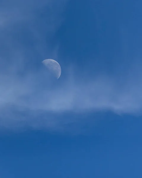 The waning moon between clouds in a blue sky. Nature.