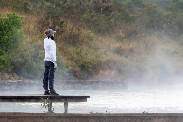 Женщина созерцает туман над озером на холодном рассвете. Стиль жизни.