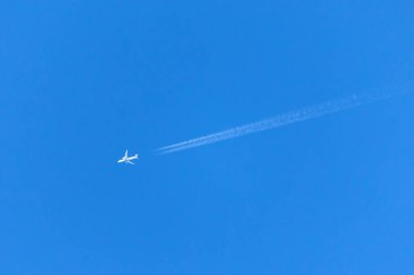 A plane crossing the blue sky leaving a white trail.