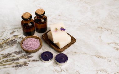 Mor mumlu lavanta tuzu ve çiçeğin üst görüntüsü, beyaz sabun ve mermer masa üzerinde bir şişe essencail yağı. Sağda Coppy alanı.