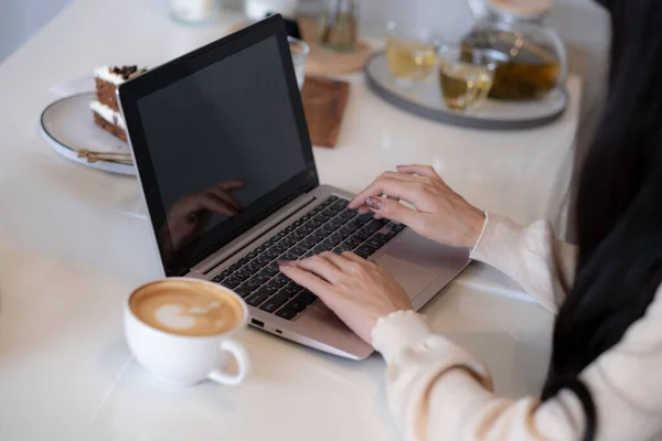 Close up of woman typing on laptop with her sweet and coffee on table, woking at home or coffee shop, business woman hand doing her work at resturant.