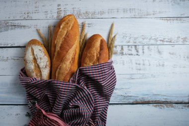 Kırmızı mor masa örtüsü ve beyaz ahşap zeminde buğday bulunan altın rengi kahverengi Fransız ekmeğinin üst görüntüsü. Sağdaki kabarık alan..