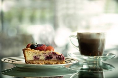 Meyveli tart keki ve cam sehpanın üzerinde bokeh arkaplanlı bir fincan bulanık kahve. kek ve kahve menüsü yatay görünüm.