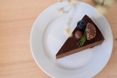 Çikolatalı keki beyaz tabakta, tahta masada, çikolata topu, yaban mersini ve üzerinde fındık ve rosmary olan çikolatayla dekore etmenin en güzel manzarası. Lezzetli ve yüksek kalorili yiyecekler..