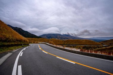 Yağmurlu bir günde Japonya 'da dağın içinden geçen yol, caddenin yanında kahverengi ve yeşil çimenler, sokaktan dağ manzarası, sokaktan dağ manzarası.