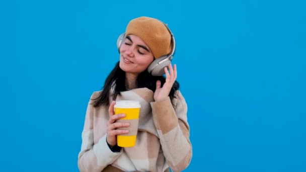 Vrouw met koptelefoon en papieren beker kijkend naar camera — Stockvideo