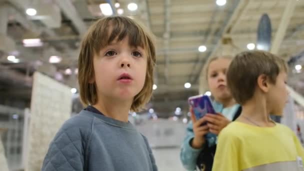 Curioso niño preescolar se encuentra en gran salón entre los niños — Vídeo de stock