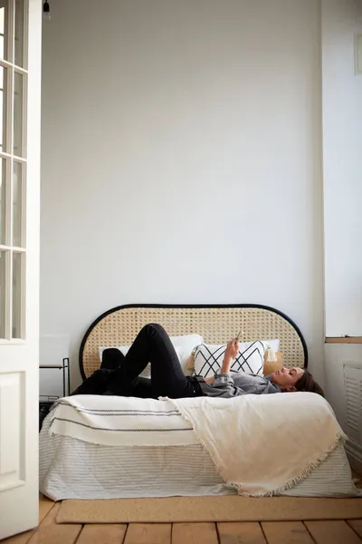 Mujer acostada en la cama y navegando teléfono inteligente — Foto de Stock