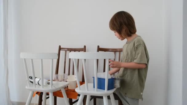 Niño pequeño juega con productos alimenticios en sillas en la habitación — Vídeos de Stock