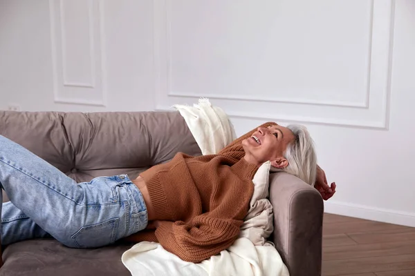 Femeia pozitivă de vârstă mijlocie râzând pe canapea Imagini stoc fără drepturi de autor