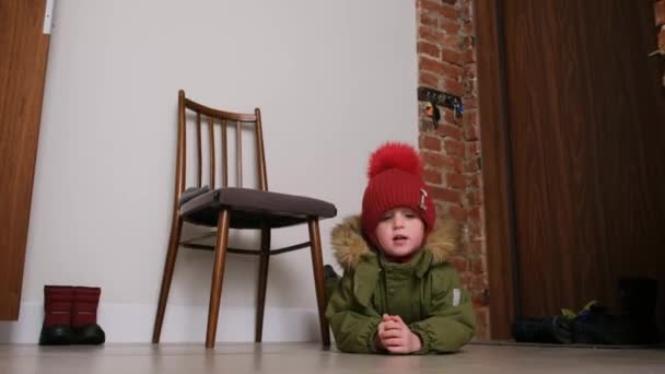 Sıcak ceketli ve kırmızı şapkalı çocuk lobide yerde yatıyor. — Stok video