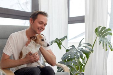 Gülümseyen adam koltukta safkan köpeği okşuyor.