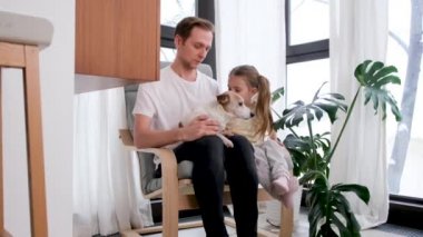 Küçük kız ve baba evde Jack Russel Terrier 'a sarılıyor.