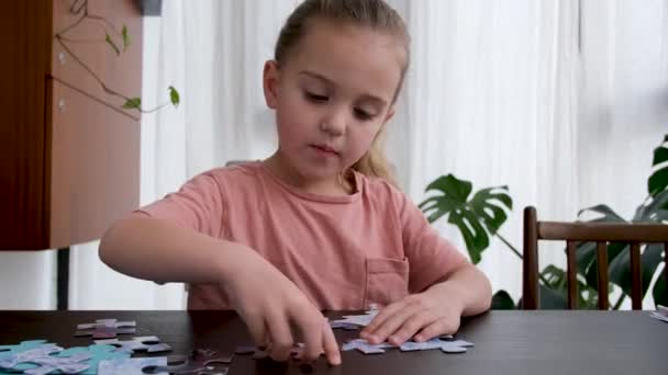 Blonde little girl does jigsaw puzzles sitting at table — Stock Video