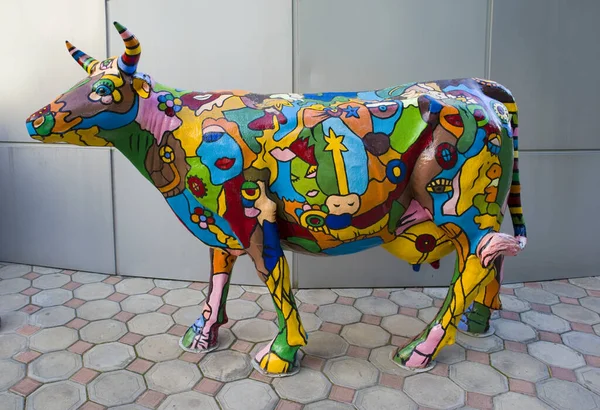 Colorful sculpture of cow with drawings on it in front of gray wall