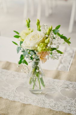 Düğün masasında şeffaf vazoda beyaz bir gül bulunan küçük bir çiçek buketi.