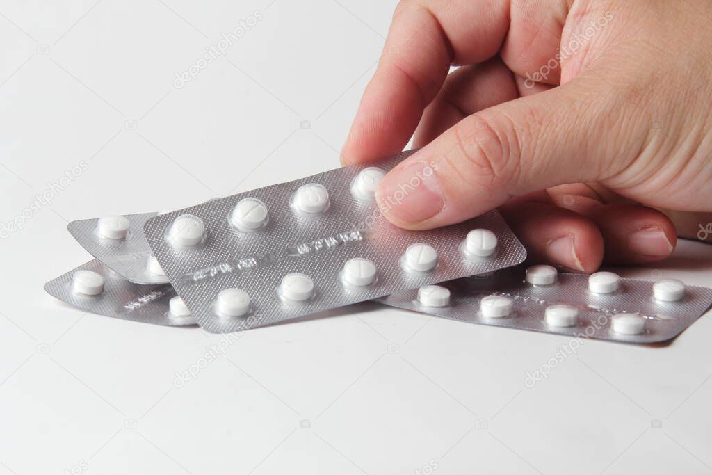 A man's hand holding pills in a pill blister on a white table.