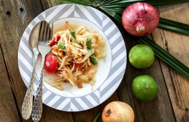 Tabakta Tayland papaya salatası, kakalı papaya salatası, limon, biber, ahşap masada beyaz kasede kırmızı domates.