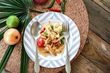 Tabakta Tayland papaya salatası, kakalı papaya salatası, limon, biber, ahşap masada beyaz kasede kırmızı domates.