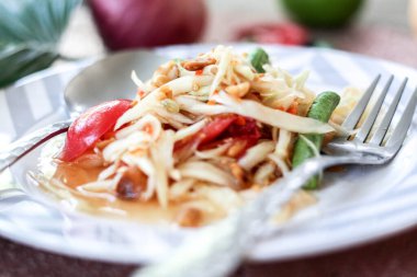 Tabakta Tayland papaya salatası, kakalı papaya salatası, limon, biber, ahşap masada beyaz kasede kırmızı domates.